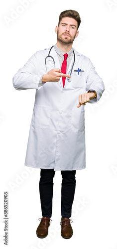 Young handsome doctor man wearing medical coat In hurry pointing to watch time, impatience, upset and angry for deadline delay