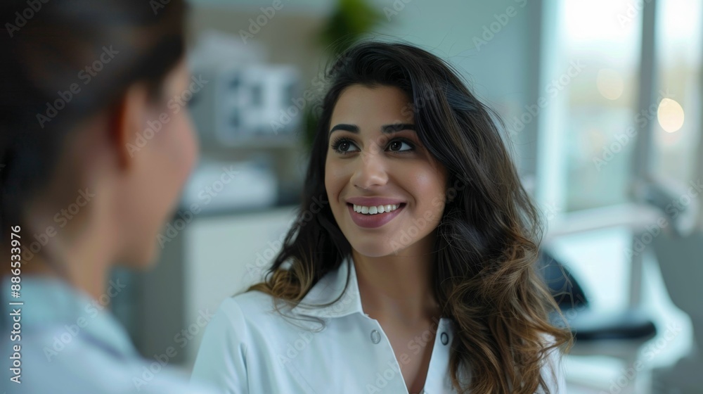 A woman with long hair smiling at another person both in a brightly lit room with a window in the background. A woman with long hair smiling at another person both in a brightly lit room with a window in the background.