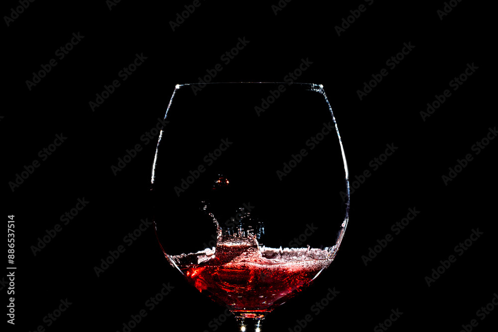 goccia che cade all'interno di un calice riempito poco con del vino rosso su sfondo nero e crea uno schizzo con forme casuali