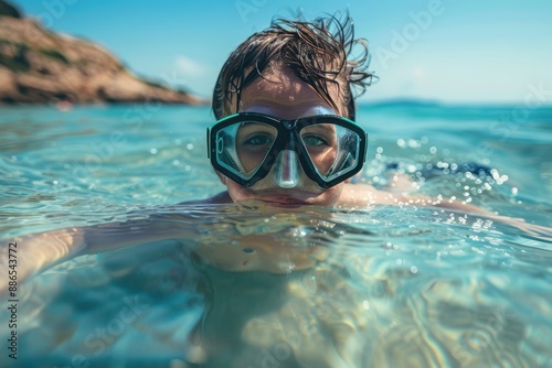 A child swims in crystal clear water near the shore, wearing blue goggles, with a scenic beach in the background on a sunny day, showcasing tranquility and fun.