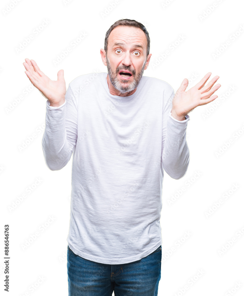 Fototapeta premium Middle age hoary senior man wearing white t-shirt over isolated background clueless and confused expression with arms and hands raised. Doubt concept.