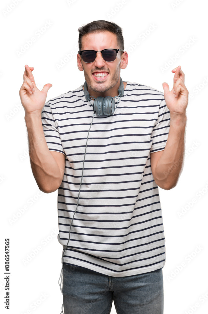 Handsome young man wearing headphones smiling crossing fingers with hope and eyes closed. Luck and superstitious concept. Handsome young man wearing headphones smiling crossing fingers with hope and eyes closed. Luck and superstitious concept.