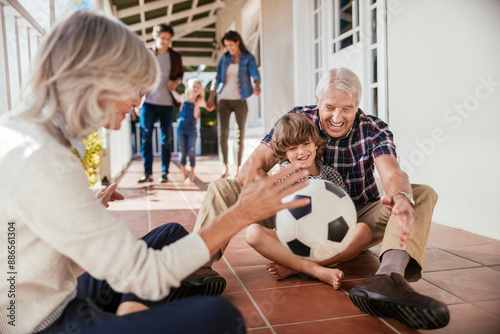 Grandparents and grandson playing with soccer ball on house porch