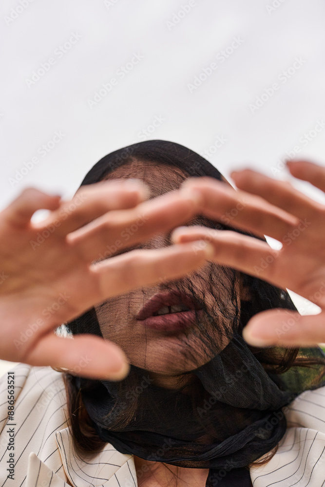 Fototapeta premium A young woman in white attire, her face covered by a veil, enjoying the summer breeze in a field of nature.