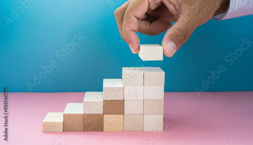 Business concept growth success process, Close up man hand arranging wood block stacking as step stair on paper blue and pink background, copy space.