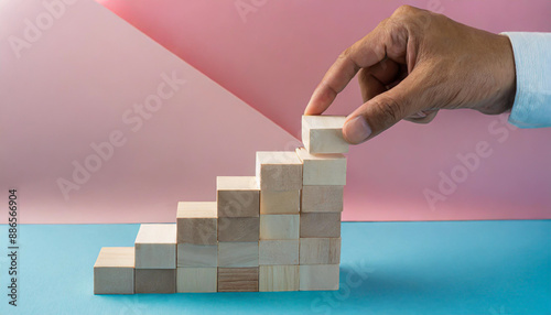 Business concept growth success process, Close up man hand arranging wood block stacking as step stair on paper blue and pink background, copy space.