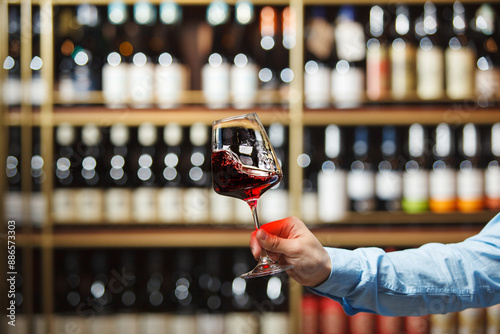 Person Holding Glass of Red Wine in Wine Store With Blurred Shelf Background