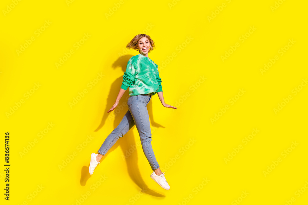Full length photo of cheerful pretty lady dressed green sweatshirt walking jumping high empty space isolated yellow color background Full length photo of cheerful pretty lady dressed green sweatshirt walking jumping high empty space isolated yellow color background