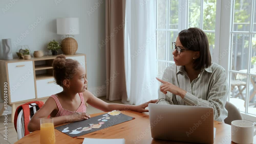 African American mother and daughter sitting at table at home. Black girl is drawing and ask mom to look, woman is working on laptop and ignores her kid, being busy African American mother and daughter sitting at table at home. Black girl is drawing and ask mom to look, woman is working on laptop and ignores her kid, being busy