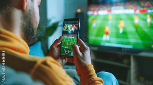 Close up of man holding smartphone with sports bets app to camera while watching football match at home copy space