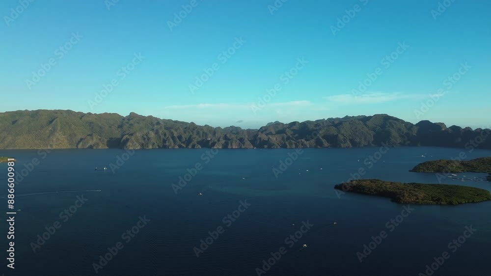 Experience a serene rightward glide over the beautiful Banuang Daan Island surrounded by the majestic mountains of Coron, Philippines. This drone footage captures the stunning interplay of sea and rug Experience a serene rightward glide over the beautiful Banuang Daan Island surrounded by the majestic mountains of Coron, Philippines. This drone footage captures the stunning interplay of sea and rug