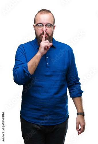 Young caucasian hipster man wearing glasses over isolated background asking to be quiet with finger on lips. Silence and secret concept.