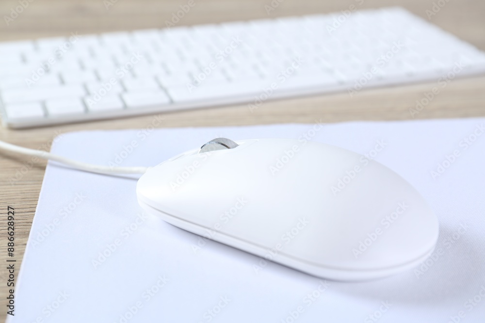 White computer mouse with mousepad and keyboard on wooden table, closeup White computer mouse with mousepad and keyboard on wooden table, closeup