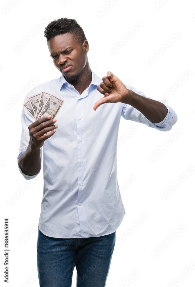Young african american businessman holding dollars with angry face, negative sign showing dislike with thumbs down, rejection concept Young african american businessman holding dollars with angry face, negative sign showing dislike with thumbs down, rejection concept
