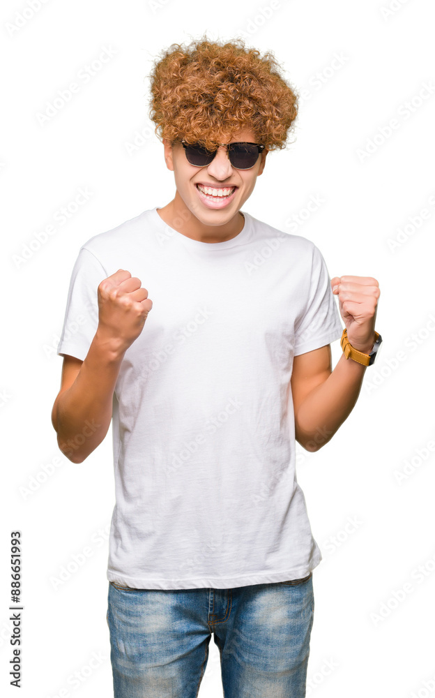 Young handsome man with afro hair wearing sunglasses very happy and excited doing winner gesture with arms raised, smiling and screaming for success. Celebration concept. Young handsome man with afro hair wearing sunglasses very happy and excited doing winner gesture with arms raised, smiling and screaming for success. Celebration concept.