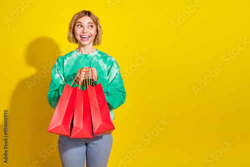 Photo of shiny attractive lady dressed tie dye sweatshirt holding bargains looking empty space isolated yellow color background