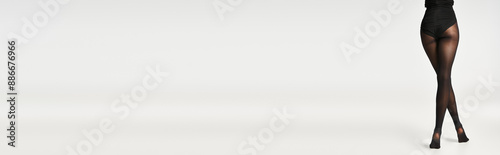 A young woman exudes sophistication in a sleek black tights against a grey studio backdrop.