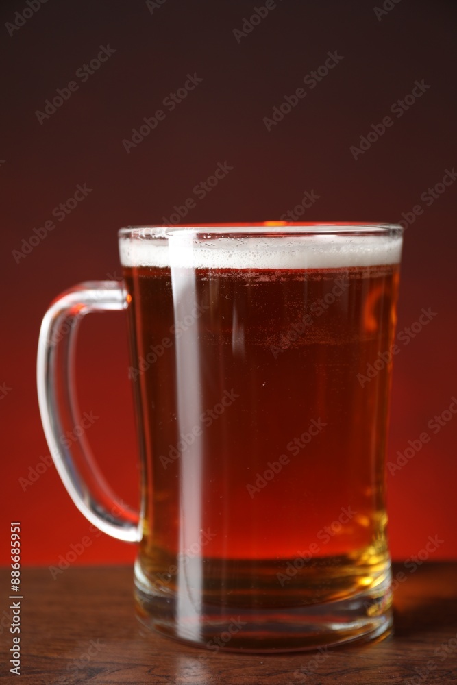 Mug with fresh beer on wooden table against color background, closeup Mug with fresh beer on wooden table against color background, closeup
