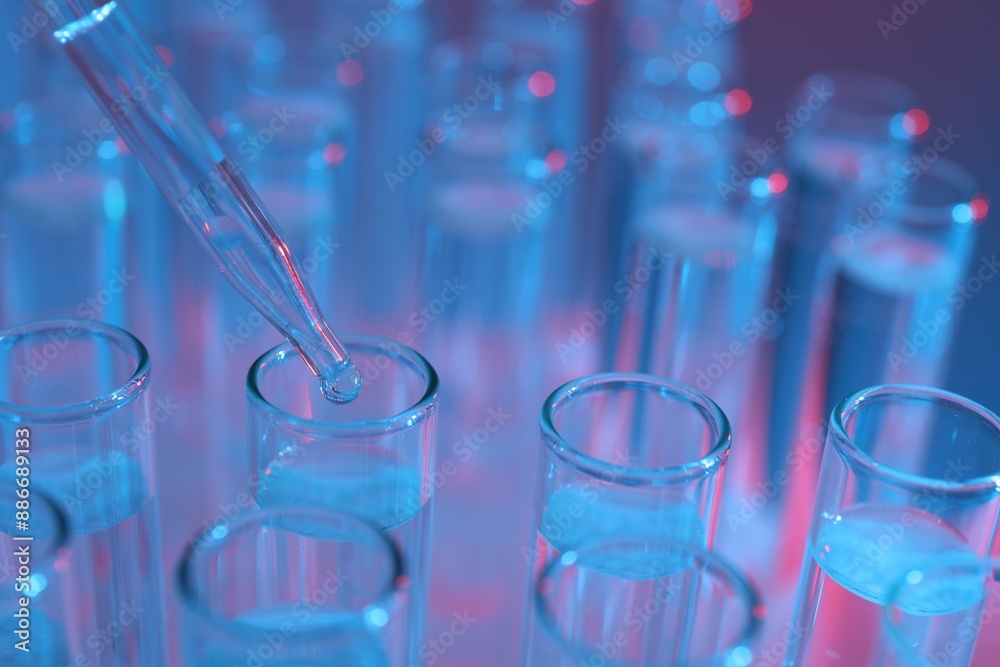 Dripping liquid from pipette into test tube on color background, closeup Dripping liquid from pipette into test tube on color background, closeup