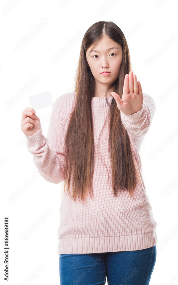 Young Chinese woman over isolated background holding visit card with open hand doing stop sign with serious and confident expression, defense gesture Young Chinese woman over isolated background holding visit card with open hand doing stop sign with serious and confident expression, defense gesture