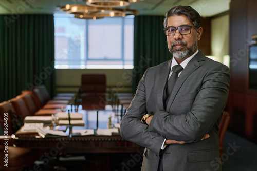 Serious mature male director of business company keeping arms crossed by chest while standing in boardroom and looking at camera
