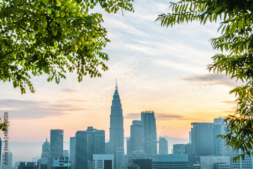 Photography Kuala Lumpur city skyline with high-rise buildings and skyscrapers in frame of green plants at sunrise, Malaysia