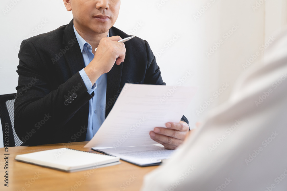 Employer or recruiter holding reading a resume during his profile of candidate, employer in suit is conducting a job interview Employer or recruiter holding reading a resume during his profile of candidate, employer in suit is conducting a job interview