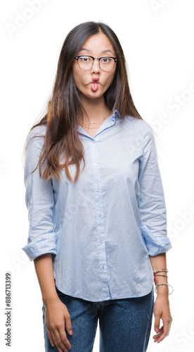 Young asian business woman wearing glasses over isolated background making fish face with lips, crazy and comical gesture. Funny expression.