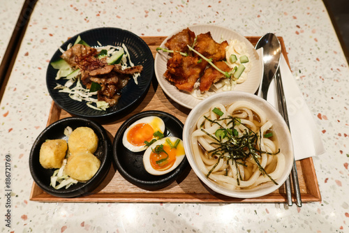 Japanese set meal with 5 different dishes including soup udon, boiled seasoned egg, stir fried pork, fried chicken and deep fried egg tofu with chopsticks and spoon photo