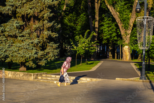 An old woman with a headscarf walks hurriedly to the park photo