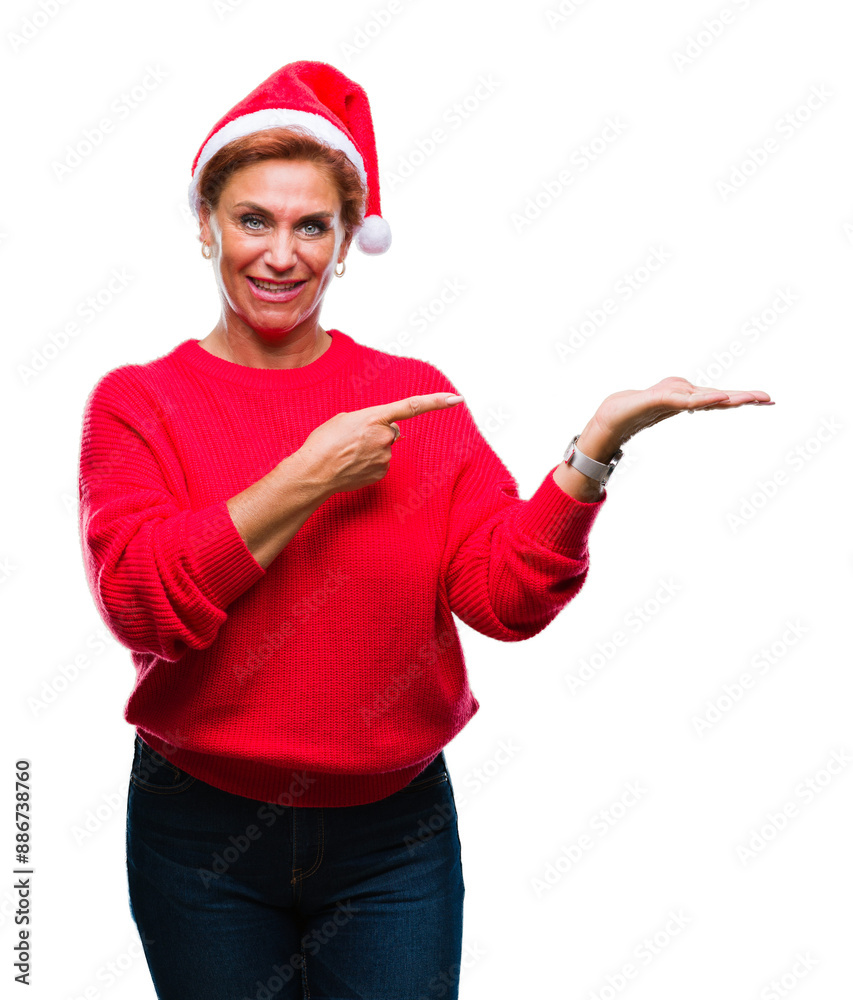 Atrractive senior caucasian redhead woman wearing christmas hat over isolated background amazed and smiling to the camera while presenting with hand and pointing with finger. Atrractive senior caucasian redhead woman wearing christmas hat over isolated background amazed and smiling to the camera while presenting with hand and pointing with finger.