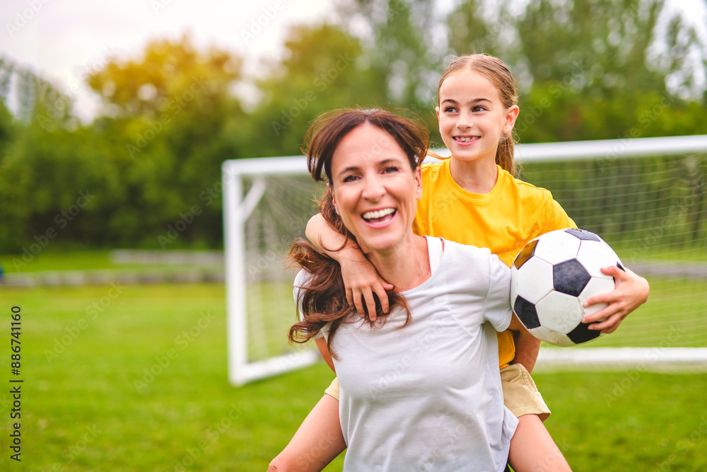 Obraz premium happy mother playing football outdoor on a summer day with her daughter