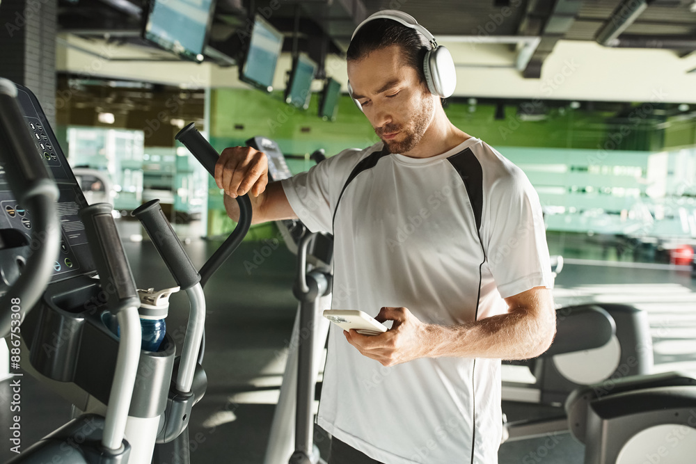 A focused man in athletic wear wearing headphones and using a cell phone while working out in a gym. A focused man in athletic wear wearing headphones and using a cell phone while working out in a gym.