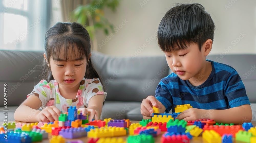 Little Asian boy and girl playing with colorful blocks on the table in their living room, stock photo style. Little Asian boy and girl playing with colorful blocks on the table in their living room, stock photo style.