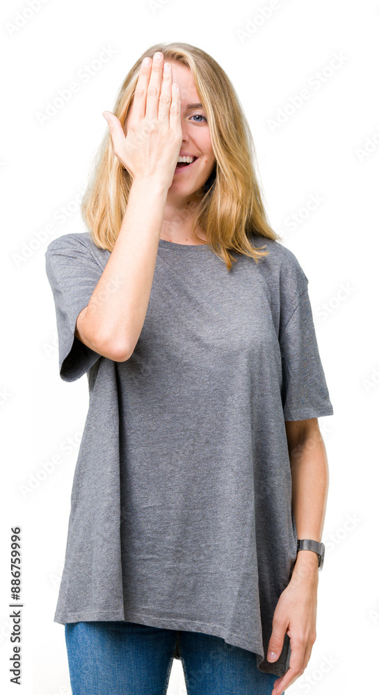 Beautiful young woman wearing oversize casual t-shirt over isolated background covering one eye with hand with confident smile on face and surprise emotion. Beautiful young woman wearing oversize casual t-shirt over isolated background covering one eye with hand with confident smile on face and surprise emotion.