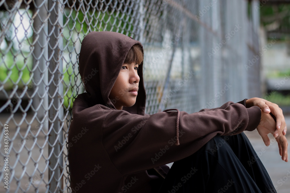 Asian pre-teen boy in a black hoodie sits with his knees pressed ...