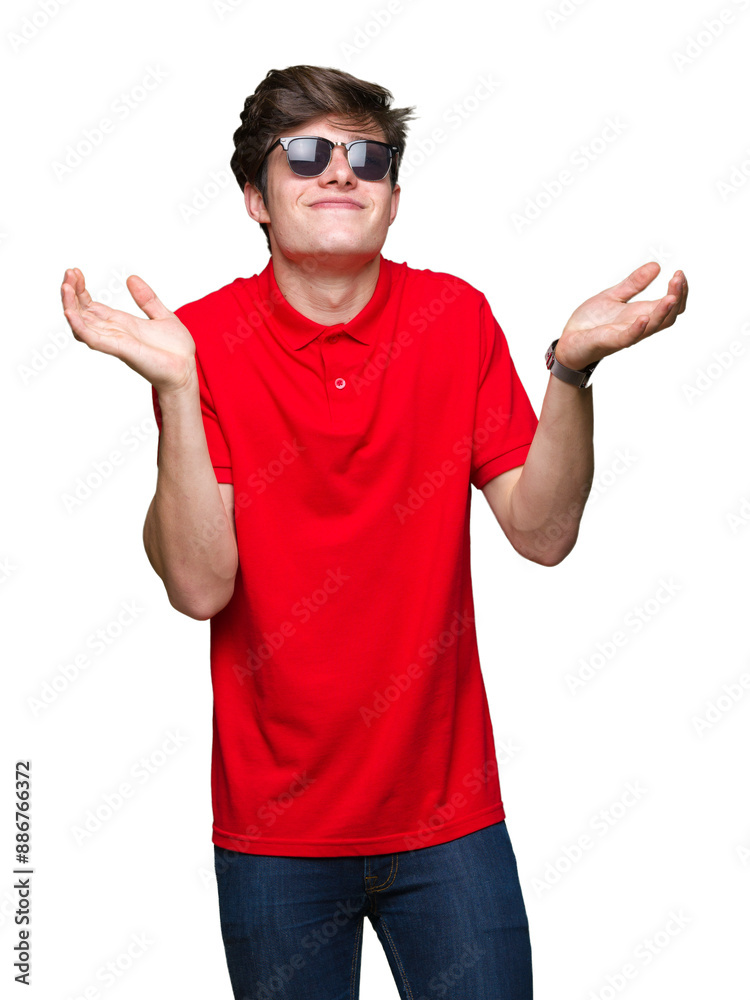 Young handsome man wearing sunglasses over isolated background clueless and confused expression with arms and hands raised. Doubt concept.