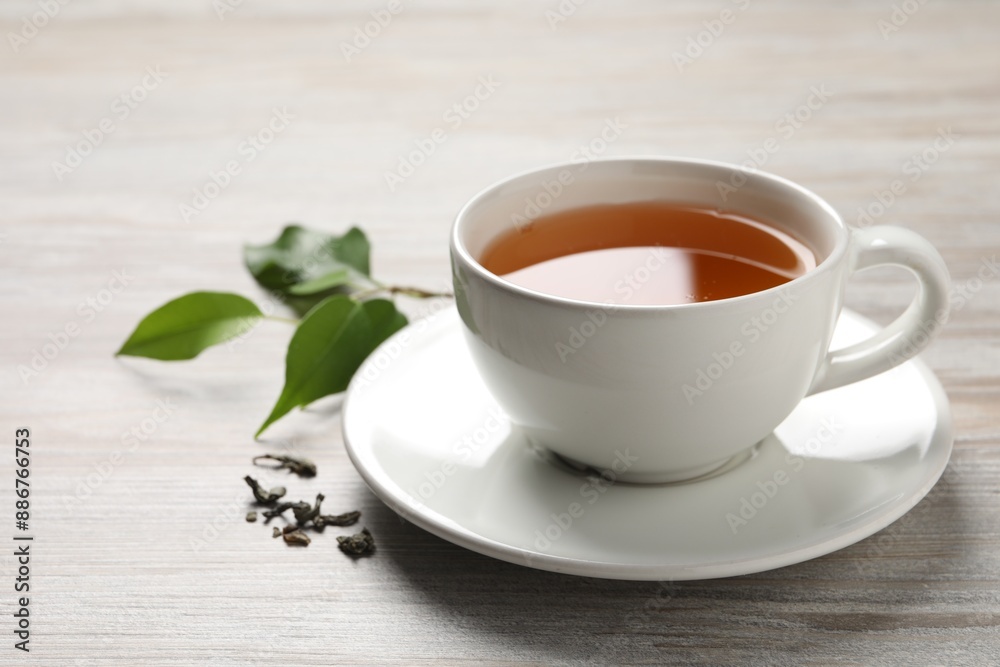 Refreshing green tea in cup and leaves on grey wooden table, closeup Refreshing green tea in cup and leaves on grey wooden table, closeup