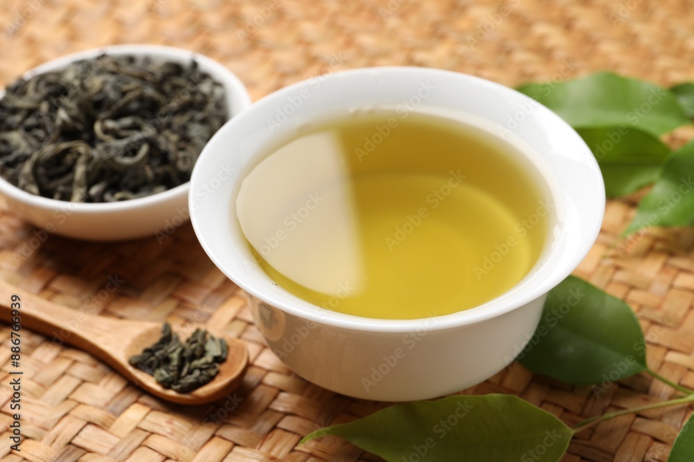 Refreshing green tea in cup, spoon and leaves on table, closeup Refreshing green tea in cup, spoon and leaves on table, closeup