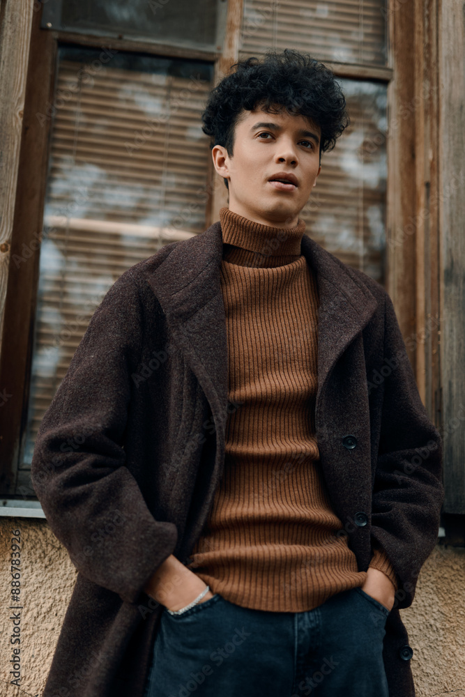 Young man in brown sweater and black jeans standing in front of an old building with wooden door and window Young man in brown sweater and black jeans standing in front of an old building with wooden door and window