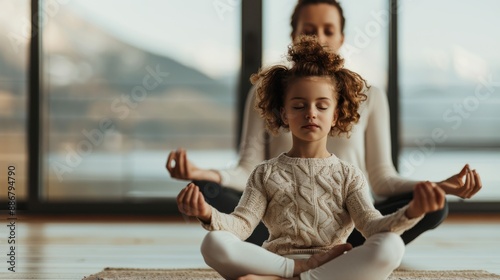 A mother and her young child are seen practicing yoga in a spacious, modern home with large windows, highlighting their focus, tranquility, and connection. photo