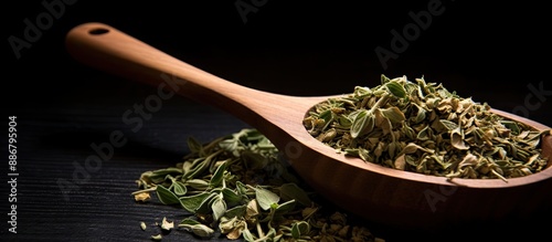 A top-down view of dried oregano herbs in a wooden spoon against a black background with a close-up shot and selective focus, offering ample copy space in the image. photo