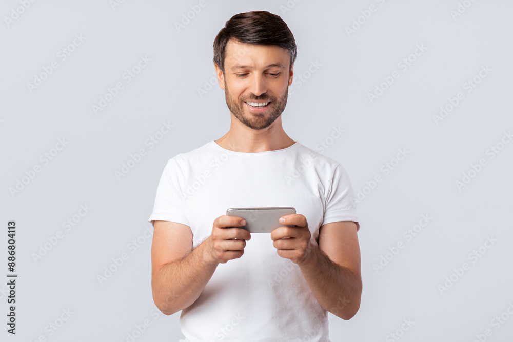 Cheerful Man Using Mobile Phone Playing Games Or Texting Over White Studio Background. Copy Space Cheerful Man Using Mobile Phone Playing Games Or Texting Over White Studio Background. Copy Space
