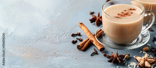 Glass cup filled with spicy warming tea, milk, cinnamon sticks, and cloves on a light gray blue surface with copy space image. photo