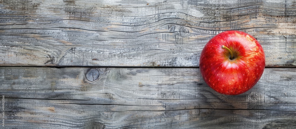 A vibrant red apple resting on a rustic brown frame atop a gray wooden surface in a top-down view with copy space image included. A vibrant red apple resting on a rustic brown frame atop a gray wooden surface in a top-down view with copy space image included.