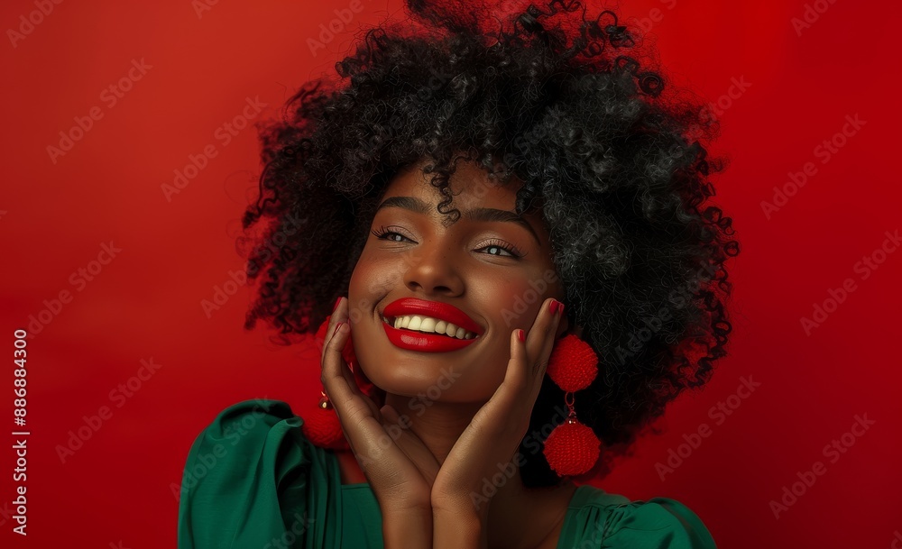Joyful woman with afro and red earrings smiling in front of red background Joyful woman with afro and red earrings smiling in front of red background