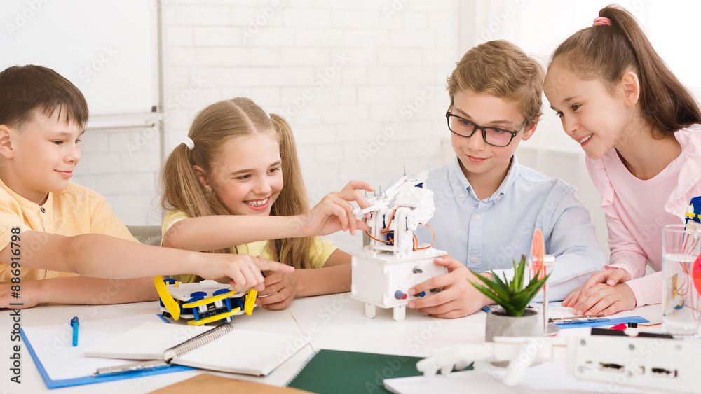 A group of children, including two girls and two boys, are working on a robotics project in a classroom setting, smiling and appear to be enjoying themselves as they learn and build together. A group of children, including two girls and two boys, are working on a robotics project in a classroom setting, smiling and appear to be enjoying themselves as they learn and build together.
