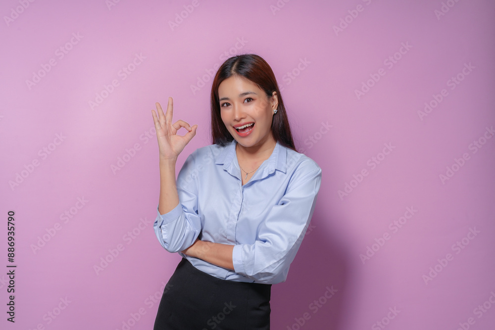 Confident young asian businesswoman smiles and shows the ok sign against a pink background, radiating positivity and approval Confident young asian businesswoman smiles and shows the ok sign against a pink background, radiating positivity and approval