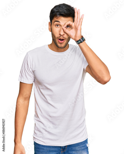 Young handsome man wearing casual white tshirt doing ok gesture shocked with surprised face, eye looking through fingers. unbelieving expression.