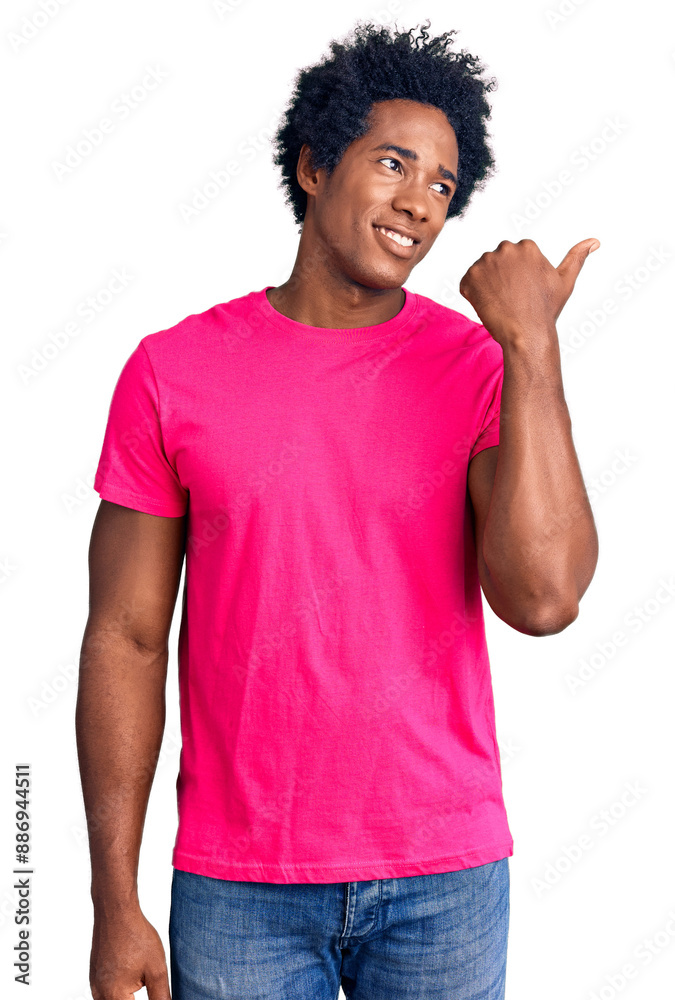 Handsome african american man with afro hair wearing casual pink tshirt smiling with happy face looking and pointing to the side with thumb up.